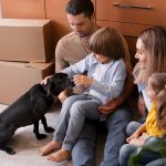 family of four, including two kids and a dog, sitting beside moving boxes
