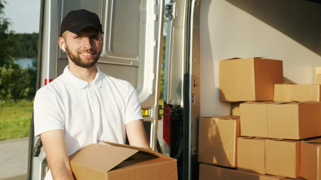 smiling mover holding a moving box, appearing to load it into a moving truck
