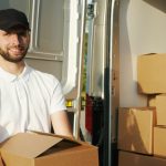 smiling mover holding a moving box, appearing to load it into a moving truck