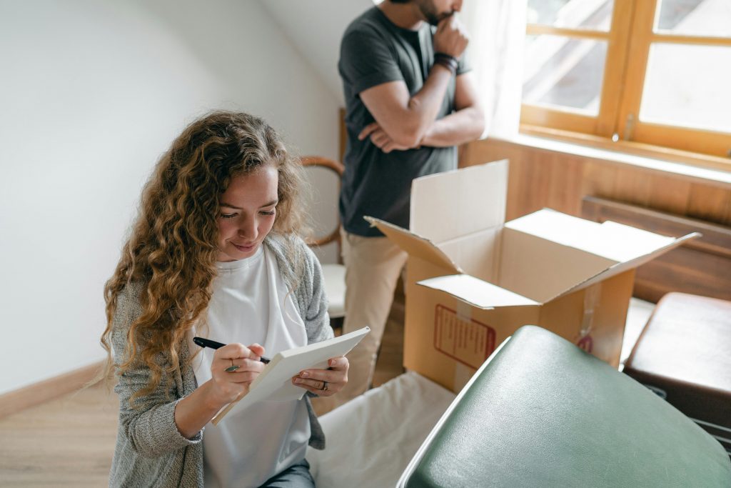 woman sitting among cardboard boxes and writing on a checklist