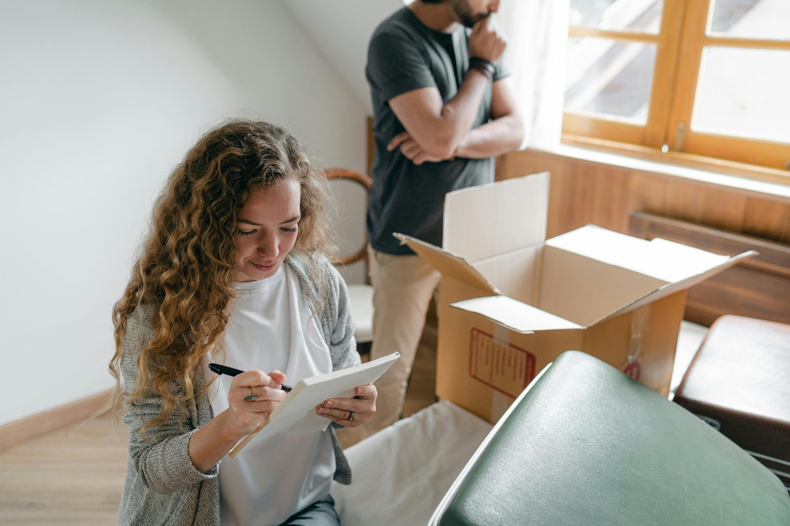 woman sitting among cardboard boxes and writing on a checklist